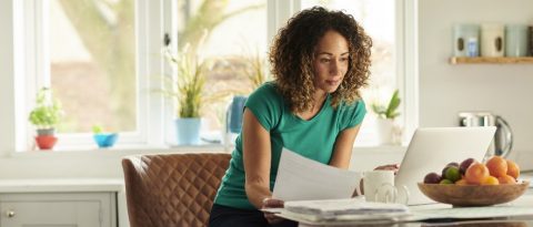 Woman viewing a paper statement and online account in her kitchen.