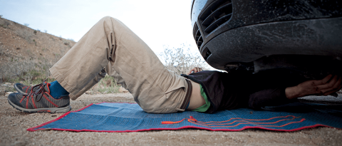 man under vehicle on roadway making repairs