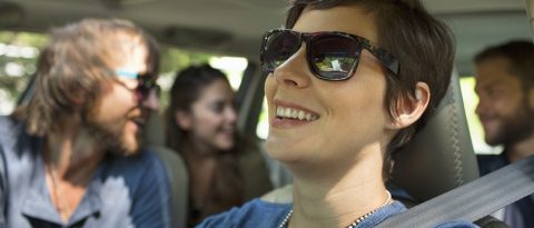 Four friends laughing in a car on a summer road trip