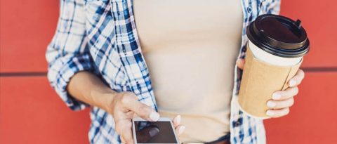 woman holding phone and coffee cup