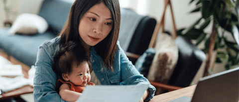 Mother examines budget while holding her infant