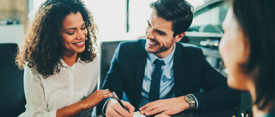 Happy couple signing a contract at a dealership.