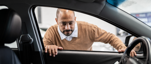 Bald man inspects the inside of a GM vehicle while pondering the true cost of vehicle ownership.